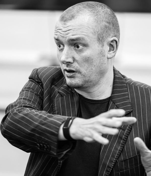 A black and white photo of a Paul Birch in a striped blazer gesticulating towards someone he is directing