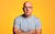 Sam Avery Sam Avery wearing a pale blue tshirt and glasses with his arms crossed against a yellowy-orange background.