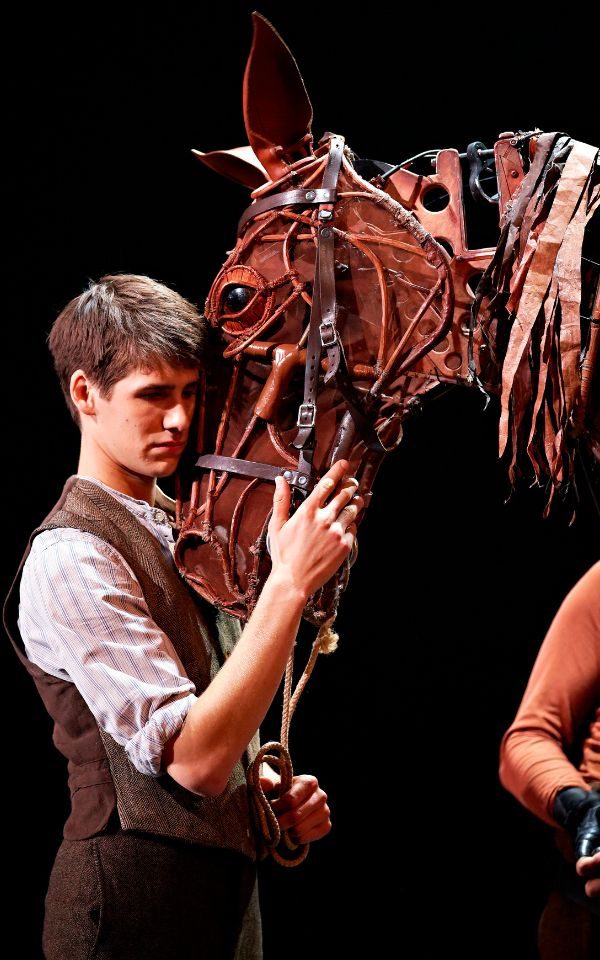 An actor in a waistcoat embracing a lifesize puppet horse's head.