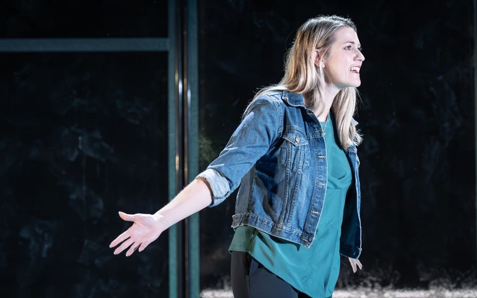 Alice Fearn as Heidi Hansen wearing a green top and denim jacket. She sings with her arm outstretched behind her.