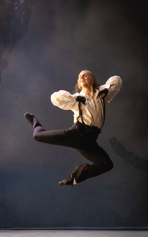 Jonathan Hanks as Scrooge leaping in the air while holding onto his braces.