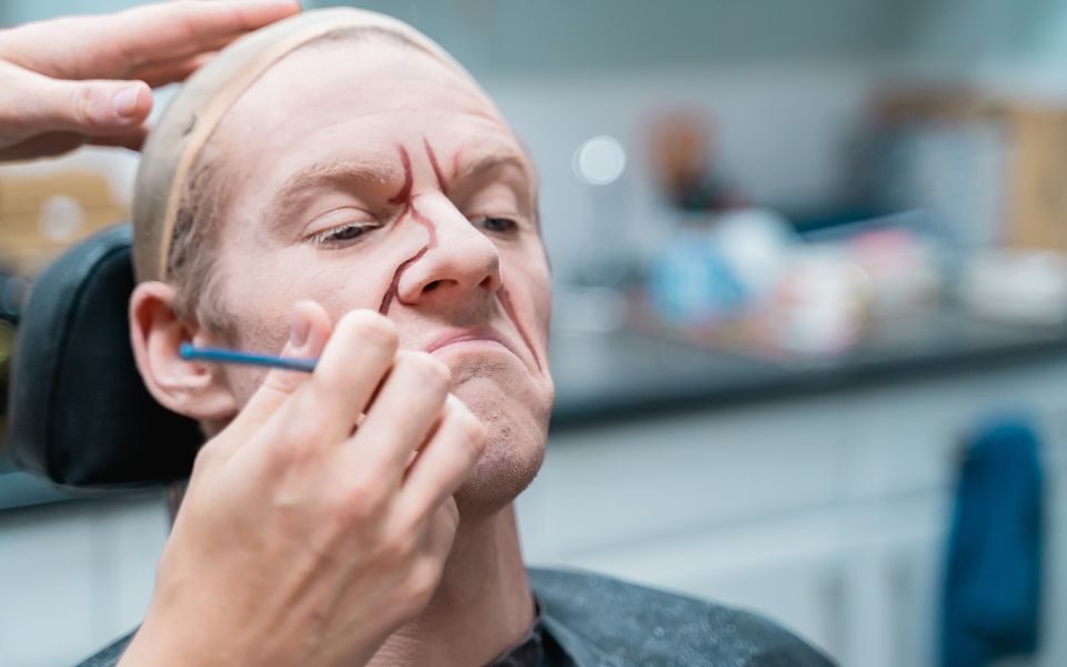 Jonathan Hanks having age lines painted on his face by Harriet Rogers.