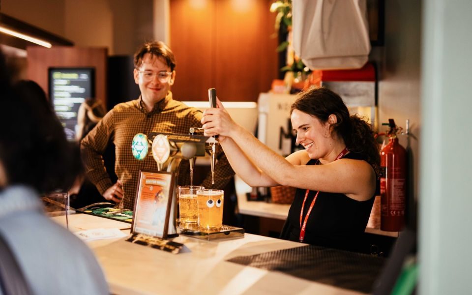 A HPPH staff member pulling two pints at the Café Bar with a colleague smiling on.