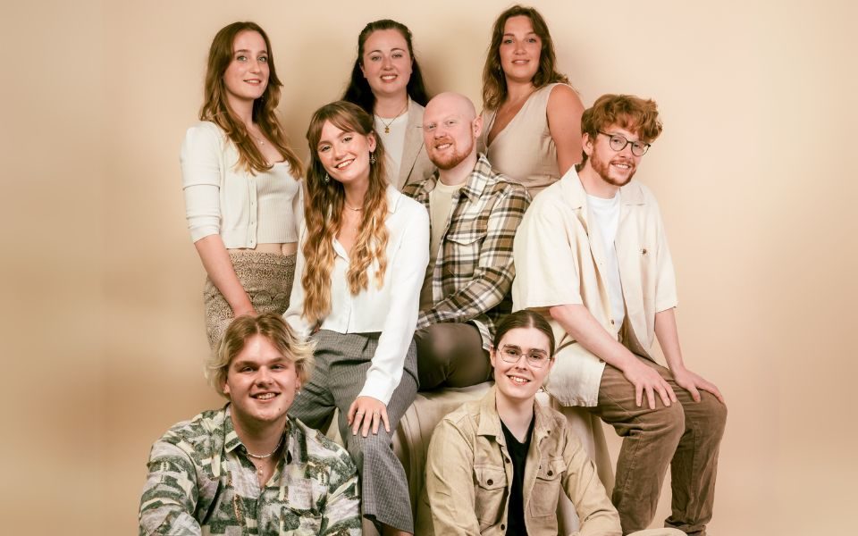 The eight members of The Apex Singers wearing neutral colours and some are wearing camo.