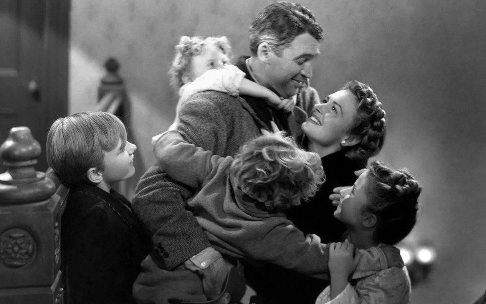 A black and white image of two parents embracing their three young children.