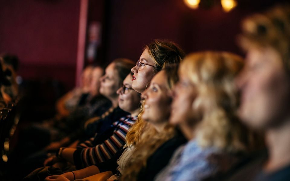 A row of audience members taken from their right side with one in the middle being the only one in focus.