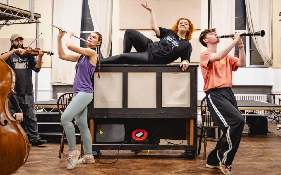 Carrie Hope Fletcher lies on top of a piano while Theo Diedrick and Emma Jane Morton play the clarinet and flute on either side of her.