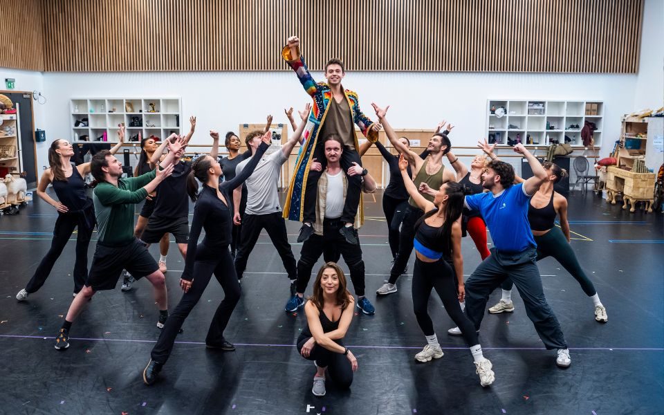 The cast of Joseph and the Amazing Technicolor Dreamcoat lifting up Adam Felipe who holds a lantern. Christina Bianco kneels down at the front of the group.