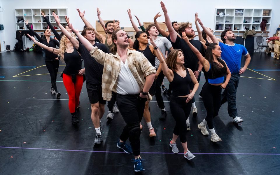 The cast of Joseph in a group with their right arms outstretched in a dance routine during rehearsals.