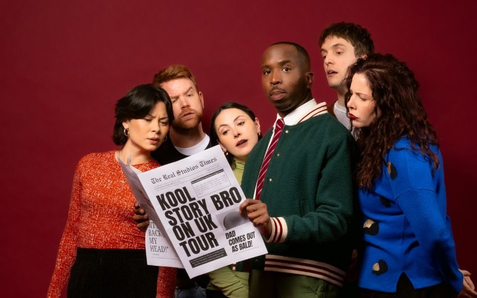 Kiell-Smith Bynoe holding a newspaper with the front page headline that reads Kool Story Bro on UK Tour. He is surrounded by other comedians including Emma Sidi, Lola-Rose Maxwell, Nic Sampson, Graham Dickson and Anna Leong Brophy trying to get a peek at the newspaper or staring at Kiell.