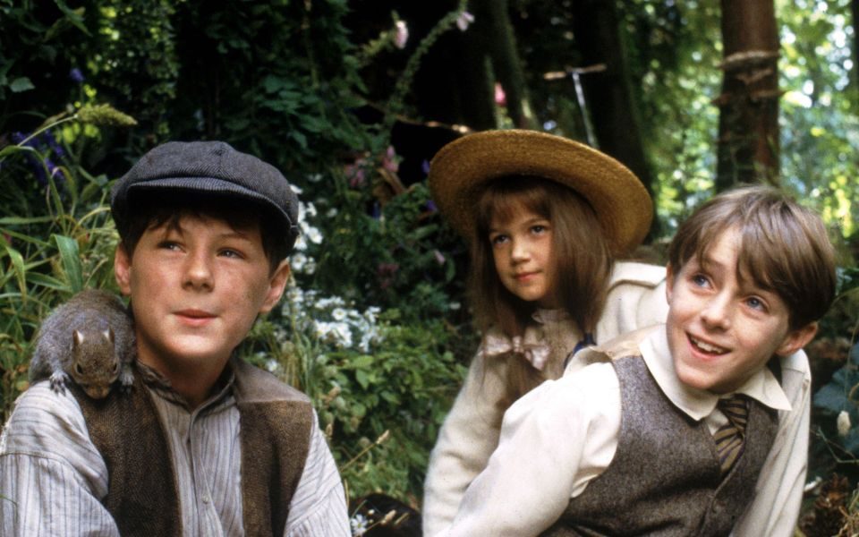 Three children in a forest, two are wearing hats and one has a squirrel on his shoulder.