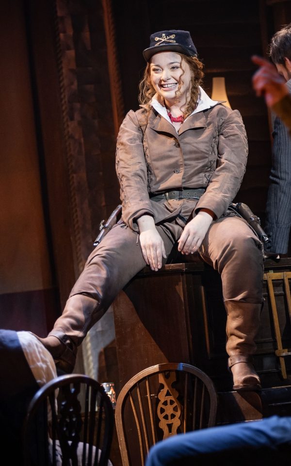 Carrie Hope Fletcher as Calamity Jane in a wild west costume and sitting on a piano.