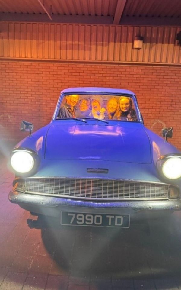 Imogen and friends posing smiling in a blue Ford Anglia