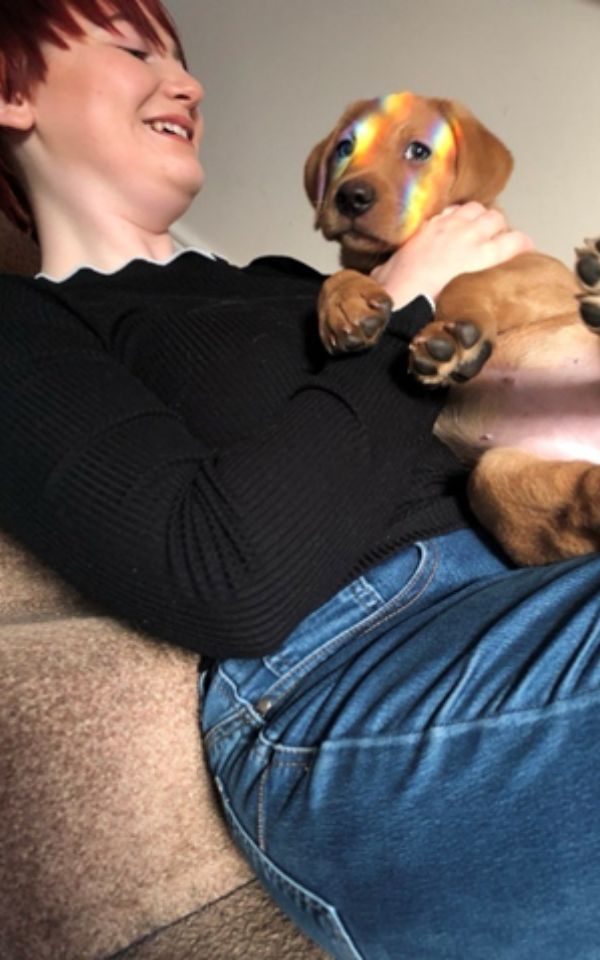 Imogen smiling holding a puppy as rainbows wash over her