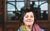 Josie Long Josie Long wearing a lovely scarf smiling in front of a door with glass windows.