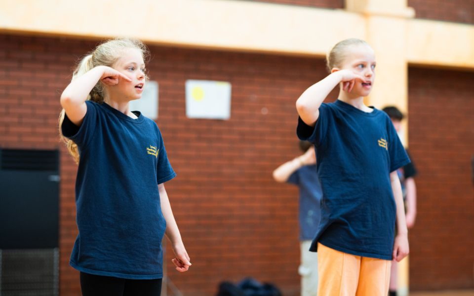 Two children in LHT navy tops in the Leeds Grand Theatre studio holding their hands to their ears as if on the phone