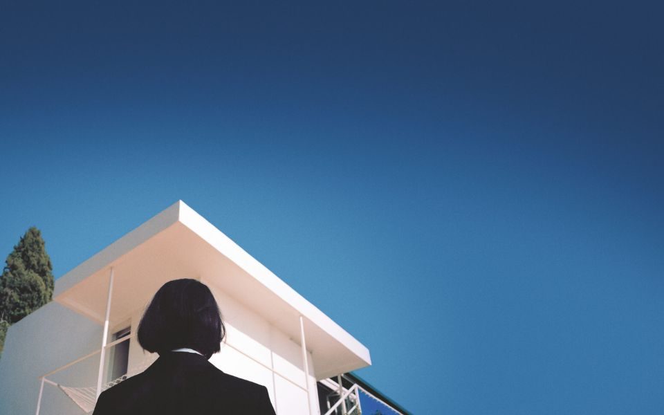 The back of someone's head who is looking up at a blue sky and a very white building.
