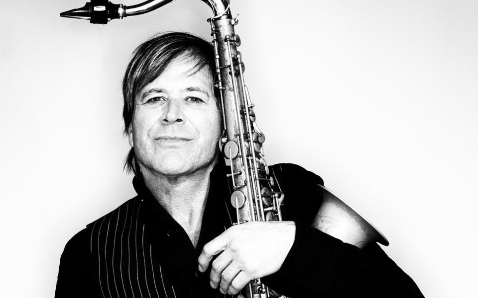 Steve Norman in black and white hugging a saxophone.