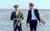 The Marching Band Two men on a beach. One is in marching band uniform, the other in a black suit with no tie.