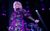 Toyah Toyah on stage in a pinky-purply shiny dress pushing a microphone stand out to the side.