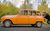 The Last Journey An elderly man driving an orange car that is being pushed by two younger men.