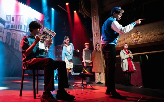 Mike Teavee sings out towards the audience with his parents, Wonka, Charlie and Cherry the reporter in the background