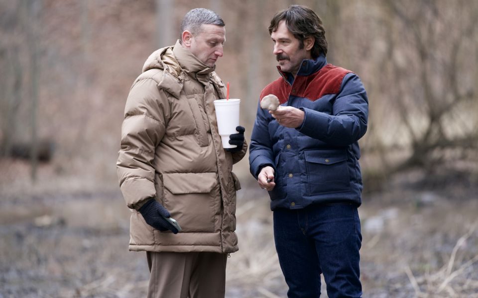 Tim Robinson and Paul Rudd converse in a wooded area, both wearing thick coats.