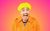 Looking For Me Friend: The Music of Victoria Wood Paulus the Cabaret Geek stands in a bright orange raincoat and yellow hat with a larger-than-life grin, wide-eyed and open-mouthed. The background is a soft pink and orange hue.