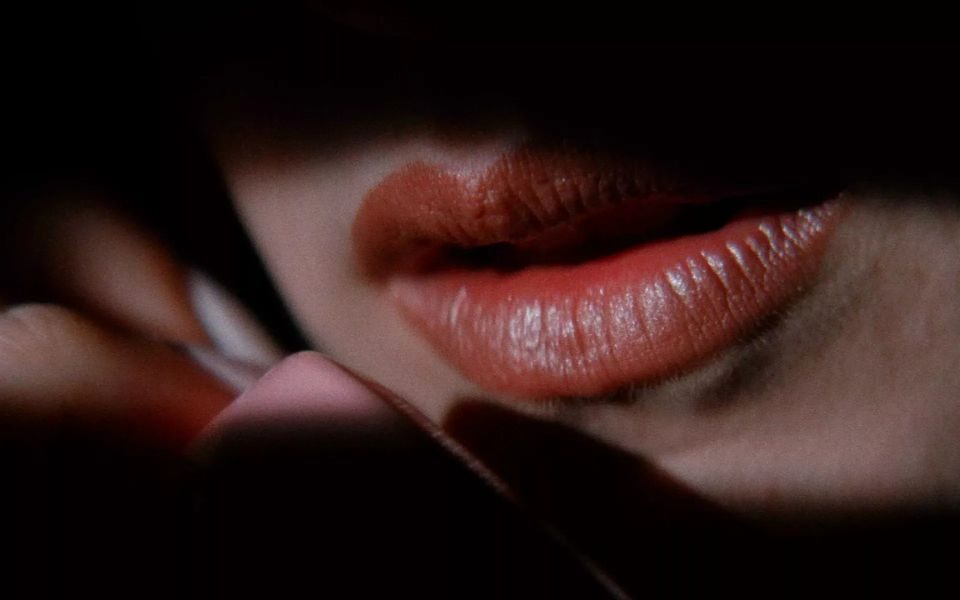 Extreme close-up of red lips next to a telephone, engulfed in stark shadow.