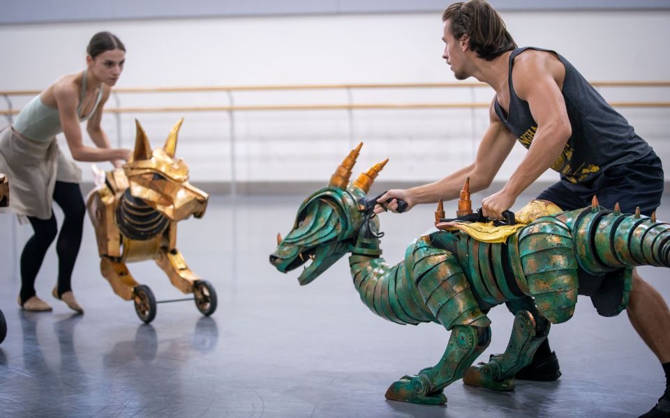 Two puppets face off in a rehearsal studio, operated by puppeteer dancers.