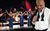 Roy Hemmings' Sounds of Philadelphia and Motown Roy Hemmings stands in the foreground in a relaxed pose, a loose bowtie round his collar and suit jacket flung on his shoulder. Three singers in sequined blue dresses stand proudly in front of a full band on-stage.