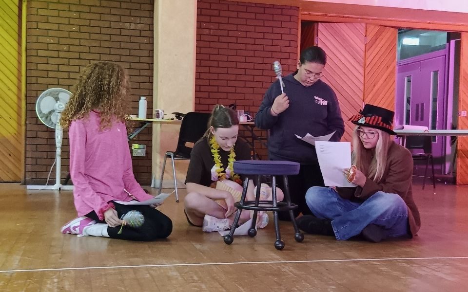 Four teenagers with hats and props perform a short piece in the Grand Studio with yellow and pink lighting