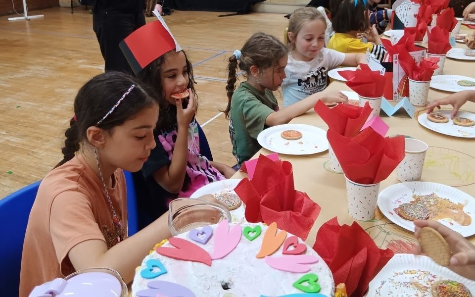 A row of children attending the LHT Unwrapped Drama Day eating their decorated biscuits at a colourful tea party table