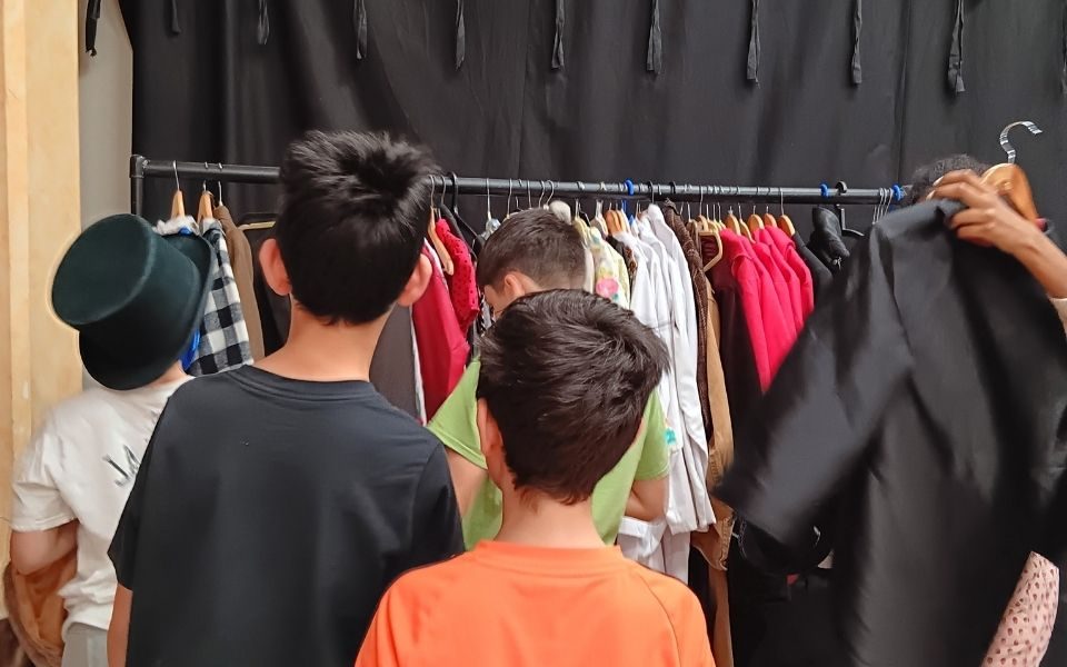 A group of boys with their backs to us pull things off the costume rail at LHT Unwrapped Drama Day