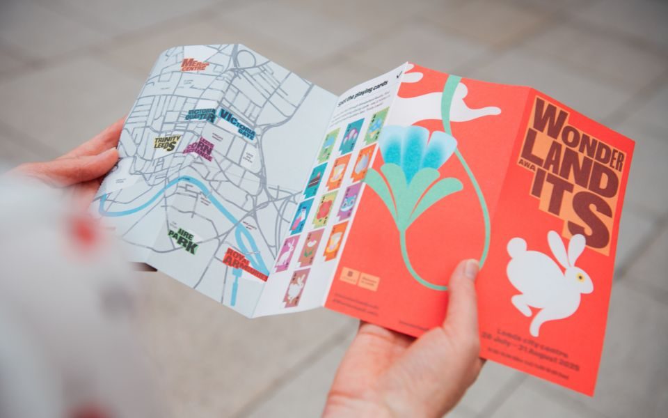 A close-up of the Wonderland Awaits trail map being opened with the red front cover and map inside visible