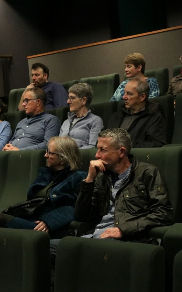 Audience members sit and listen intently in the seats of an auditorium