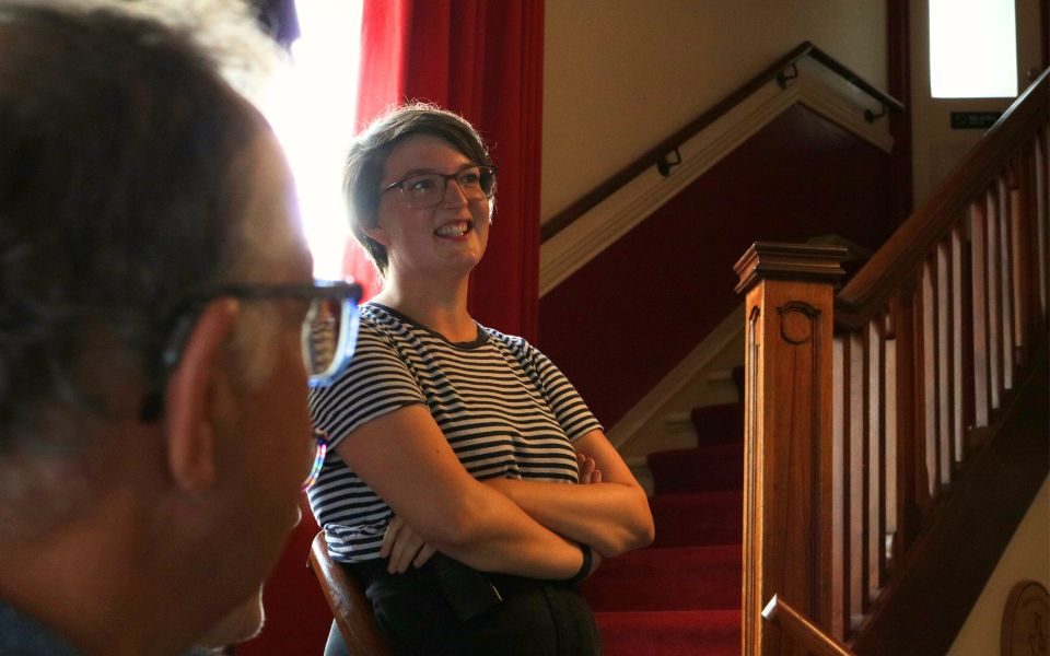 Young Audiences Officer Sylvia smiles, arms crossed, on the stairs of the Hyde Park Picture House foyer