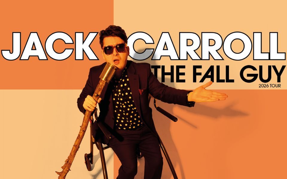 Jack Carroll in a black suit, polka dot shirt and sunglasses speaks into a tin can on a long wooden stick, his other hand outstretched, positioned in front of a orange and yellow chequered pattern. Text reads: Jack Carroll, The Fall Guy, 2026 Tour