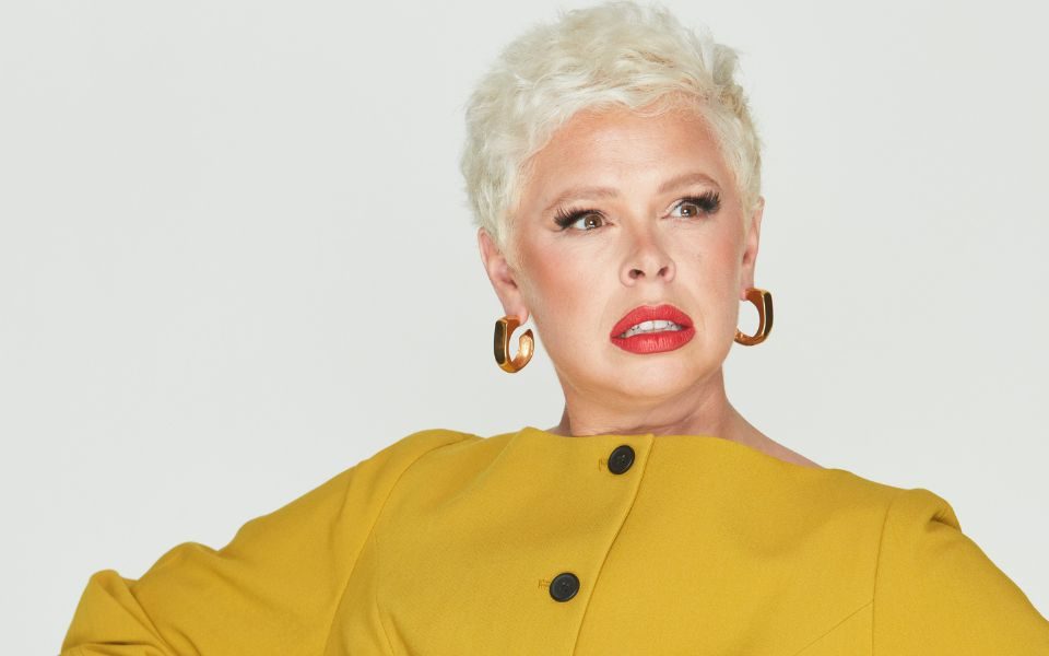 Laura Smyth looks fiercely off-camera and is wearing a yellow button-up dress, red lipstick and red nails.