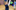 A young girl has her back to the camera and her face is turned towards it. She has a sly grin on her face. There is a cartoon green potion bottle superimposed into her hand.