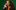 Alasdair Beckett-King's long red hair breezes over his shoulder as he holds a white telephone to his ear with a shocked expression. He wears an orange jumper and brown suit jacket, as he stands in front of a dark green background.