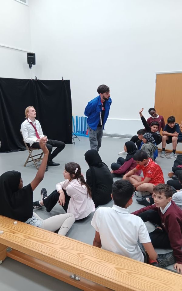A performer sat in the hot seat as Ashley delivers to a group of students sat in a hall