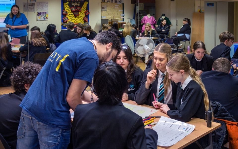 Around a table, students work on a large sheet of paper as Ashley talks to them