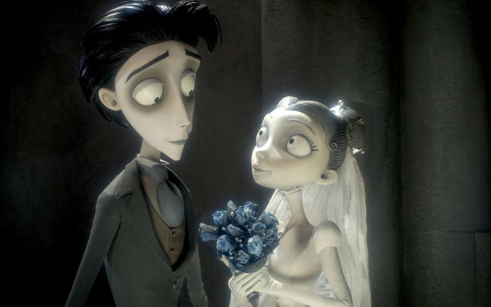 Two pale, wide-eyed animated characters look affectionately at each other, dressed in wedding garments as they stand in a gloomy room.