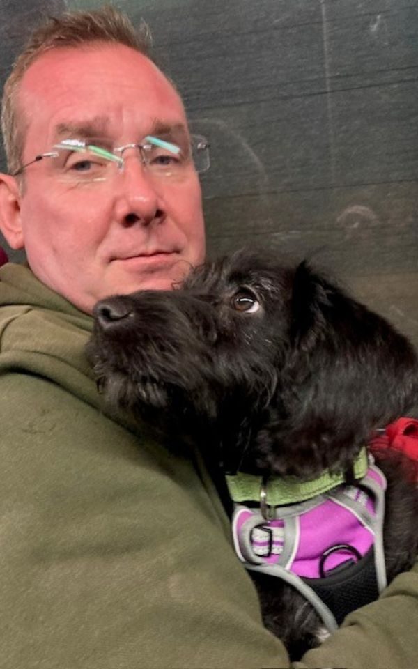 Garry Barnes holding a small black dog in his arms.
