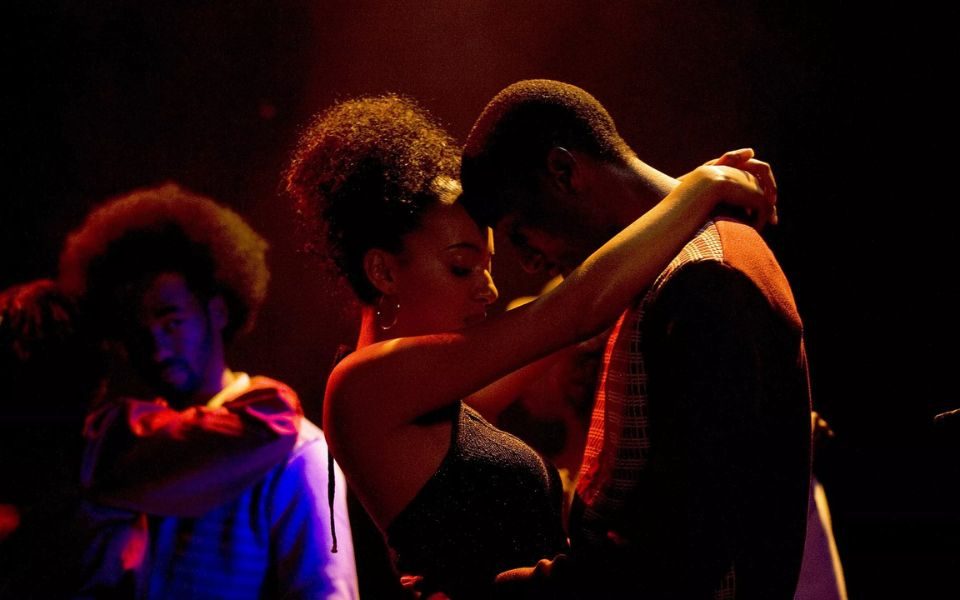 In hazy red light on the dancefloor, a couple rest their foreheads against each other's and intimately dance together.