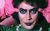 Strange Journey Tim Curry from The Rocky Horror Picture Show in close-up wearing heavy, stylised makeup and bead necklace, holds his pink gloved hands up to his head.
