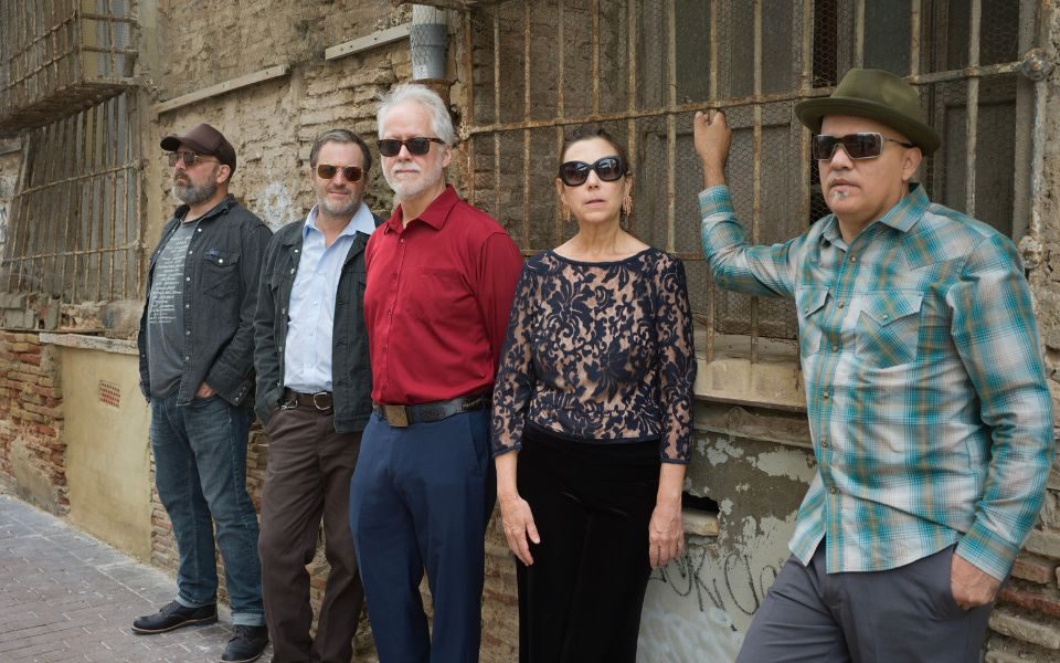 Members of The Delines all wearing sunglasses and casually posing along a brick wall.