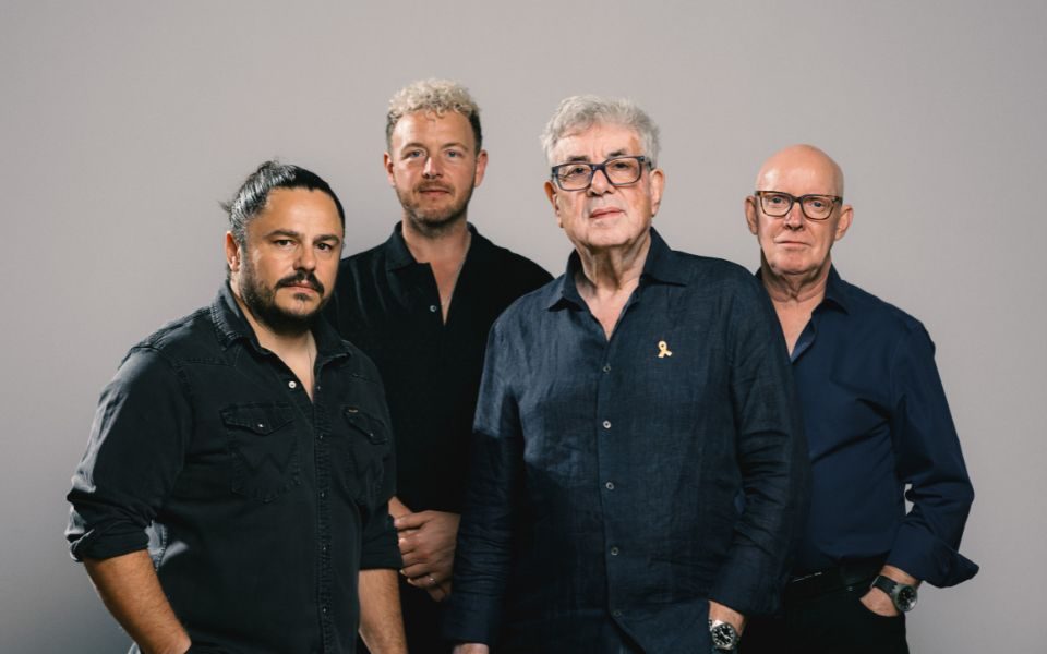 Graham Gouldman and Heart Full of Songs stand in front of a grey backdrop.