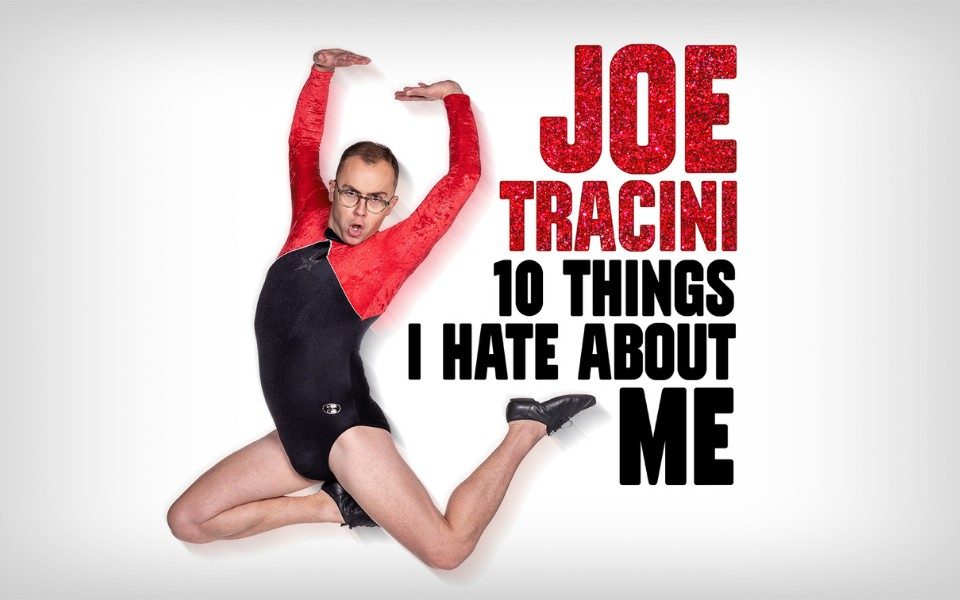 In a black and red leotard, Joe Tracini strikes a pose in mid-air with arms and legs outstretched, with an open-mouthed expression. Glittery red text reads: Joe Tracini. 10 Things I Hate About Me.